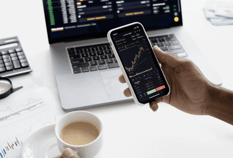 stock market on the laptop and on a mobile device and a cup of coffee and calculator next to them