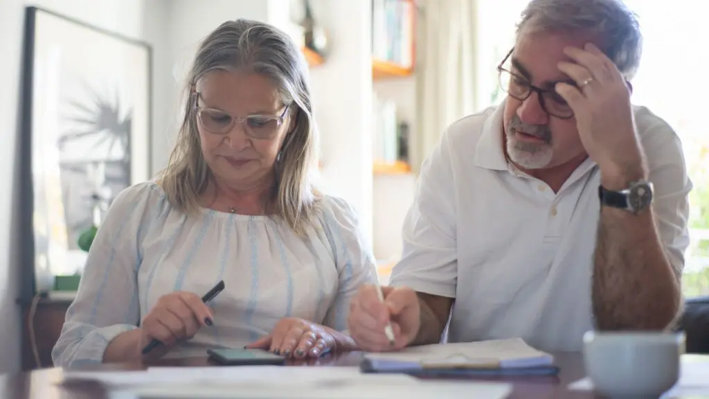 A couple in their late 50s reviewing retirement paperwork at a kitchen table