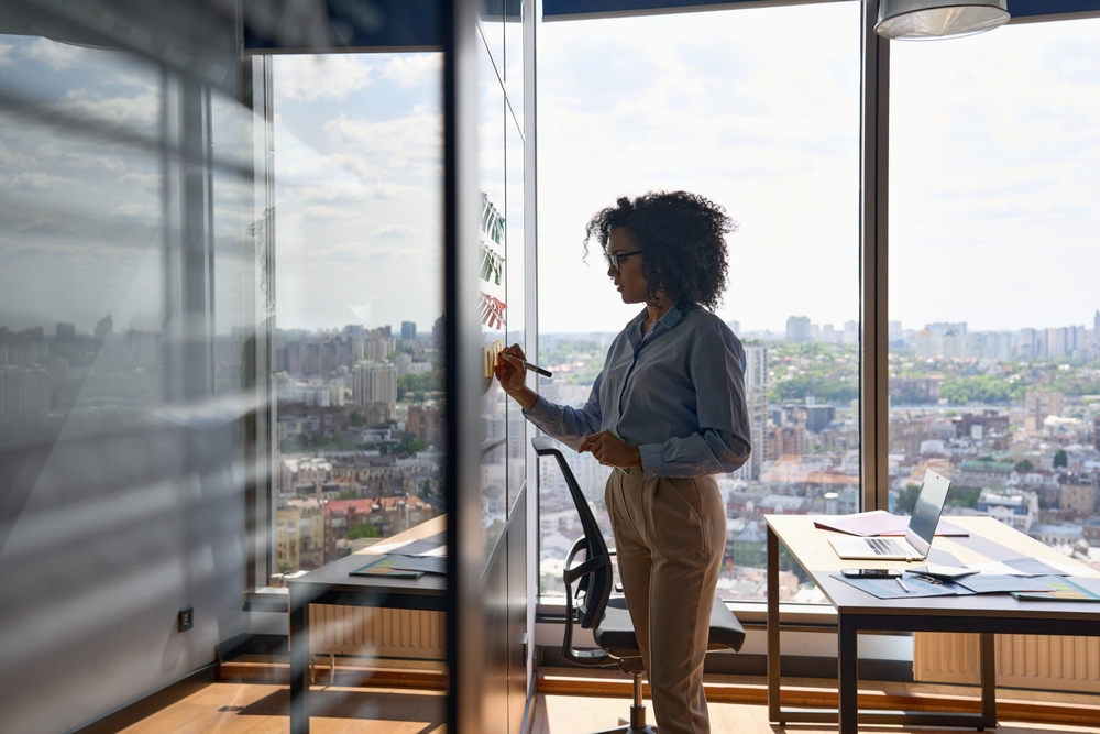 Businesswoman brainstorming ideas on a whiteboard in a modern office with a city view.