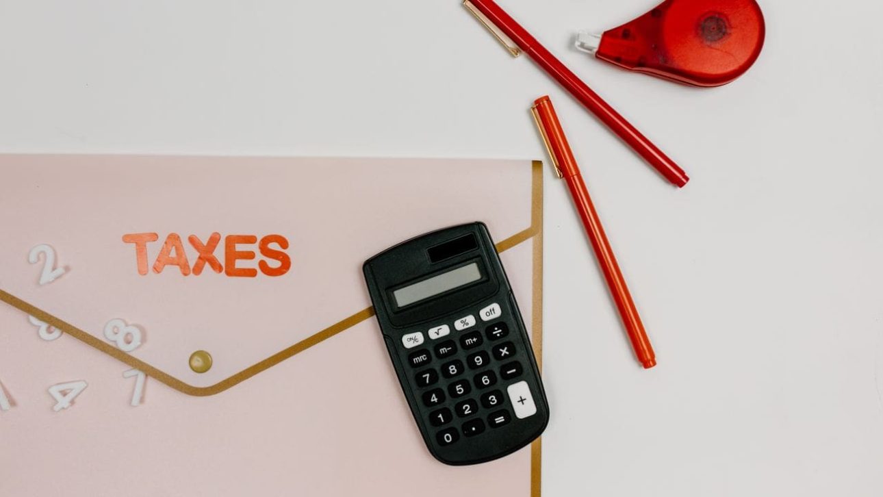 Calculator and red pens beside a folder labeled taxes, representing IRMAA and Medicare premium planning