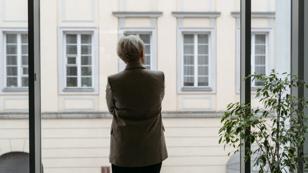 Professional woman looking out an office window, thinking about retiring at 60