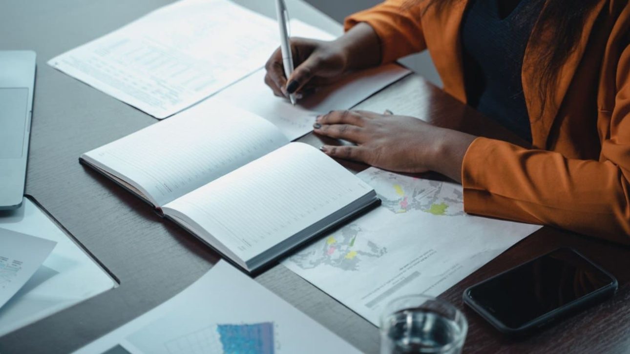 professional woman writing in a planner beside spreadsheets while mapping out her mega backdoor Roth strategy