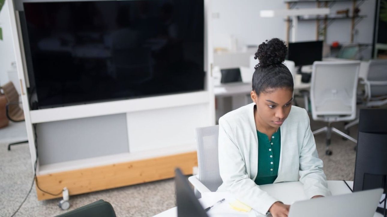 Focused professional woman in a white blazer using a laptop, reviewing her MongoDB employee benefits