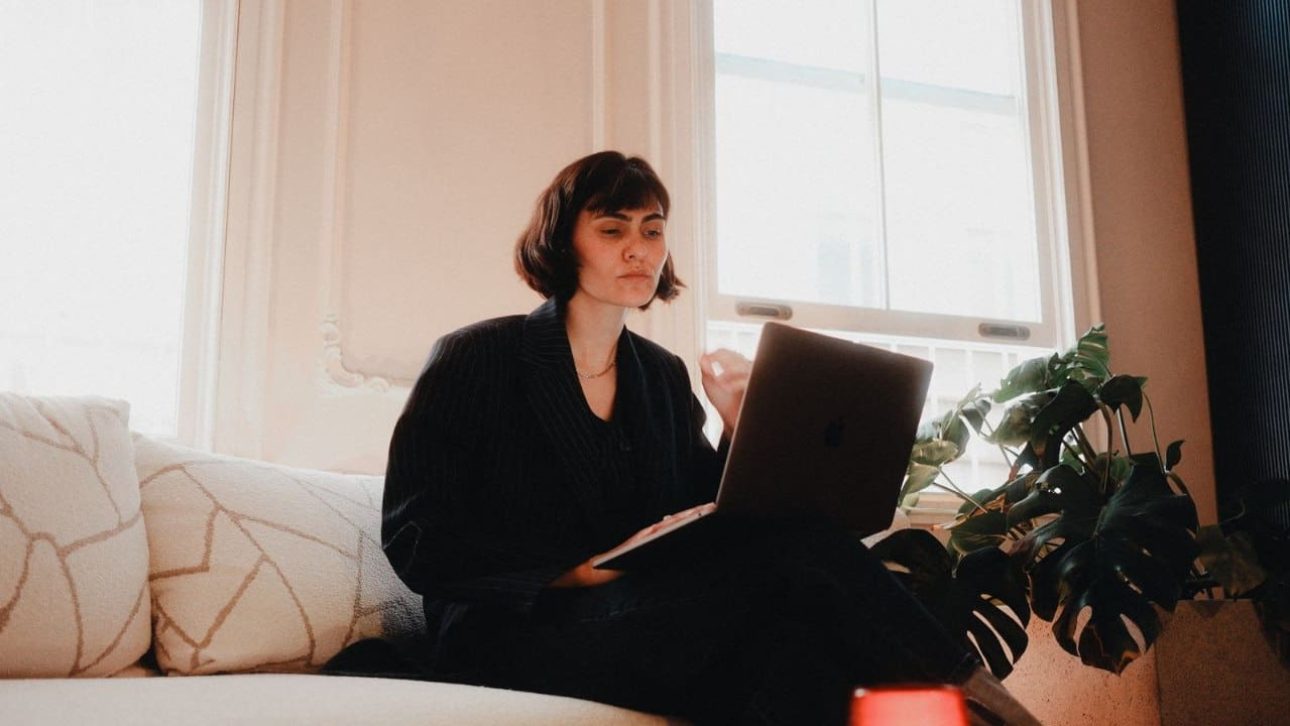 Professional woman in a suit working on a laptop from a sofa, reviewing her Netflix employee benefits