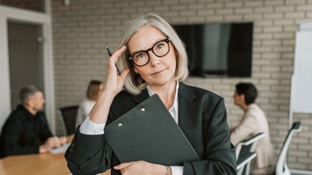 Woman executive in her 50s holding a clipboard in a meeting room, weighing a pension lump sum or annuity decision