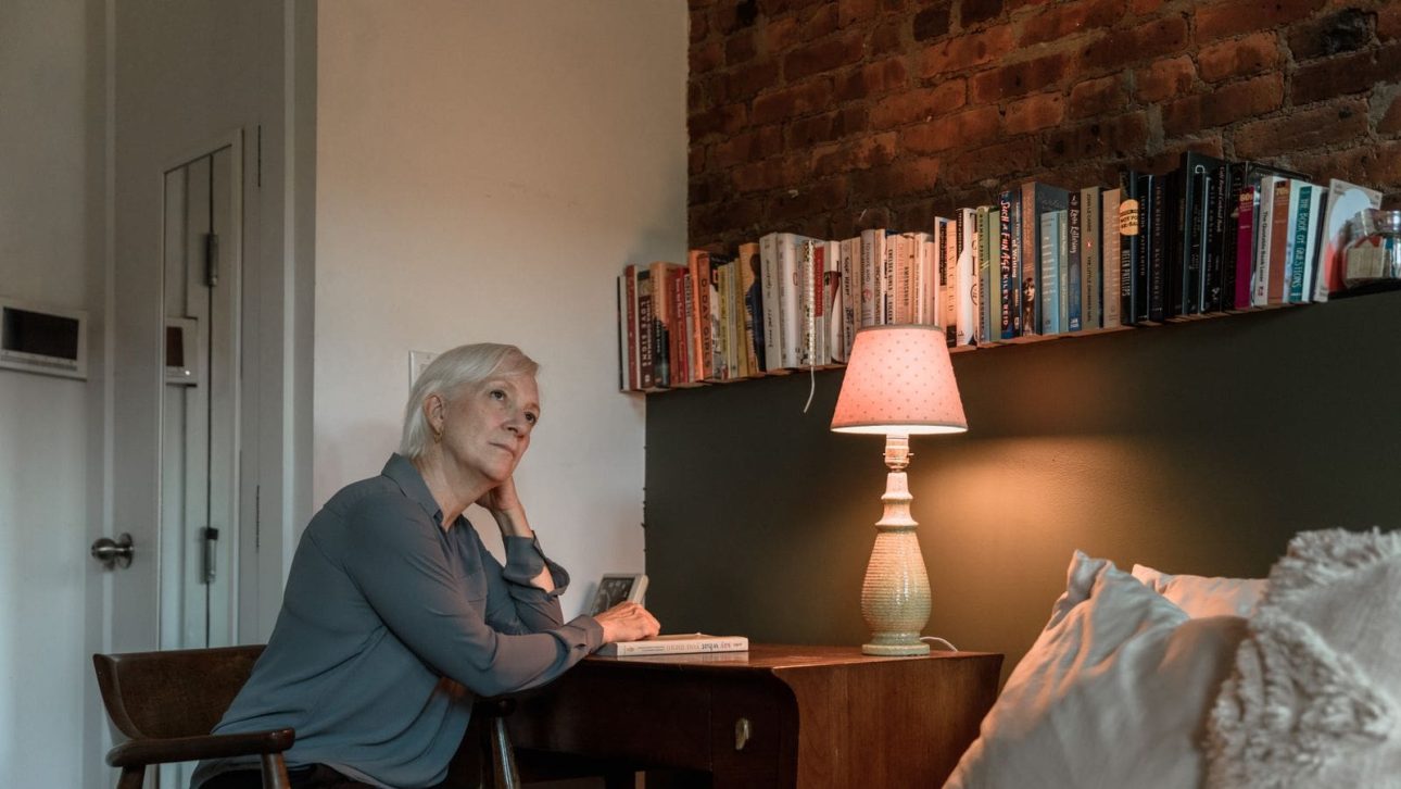 A woman in her 60s sitting at a table with papers, thinking