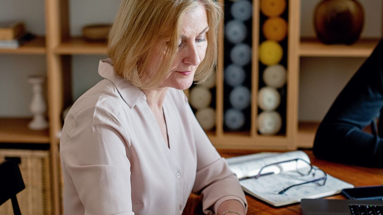A woman in her fifties at her home table, calmly writing out her first year financial checklist